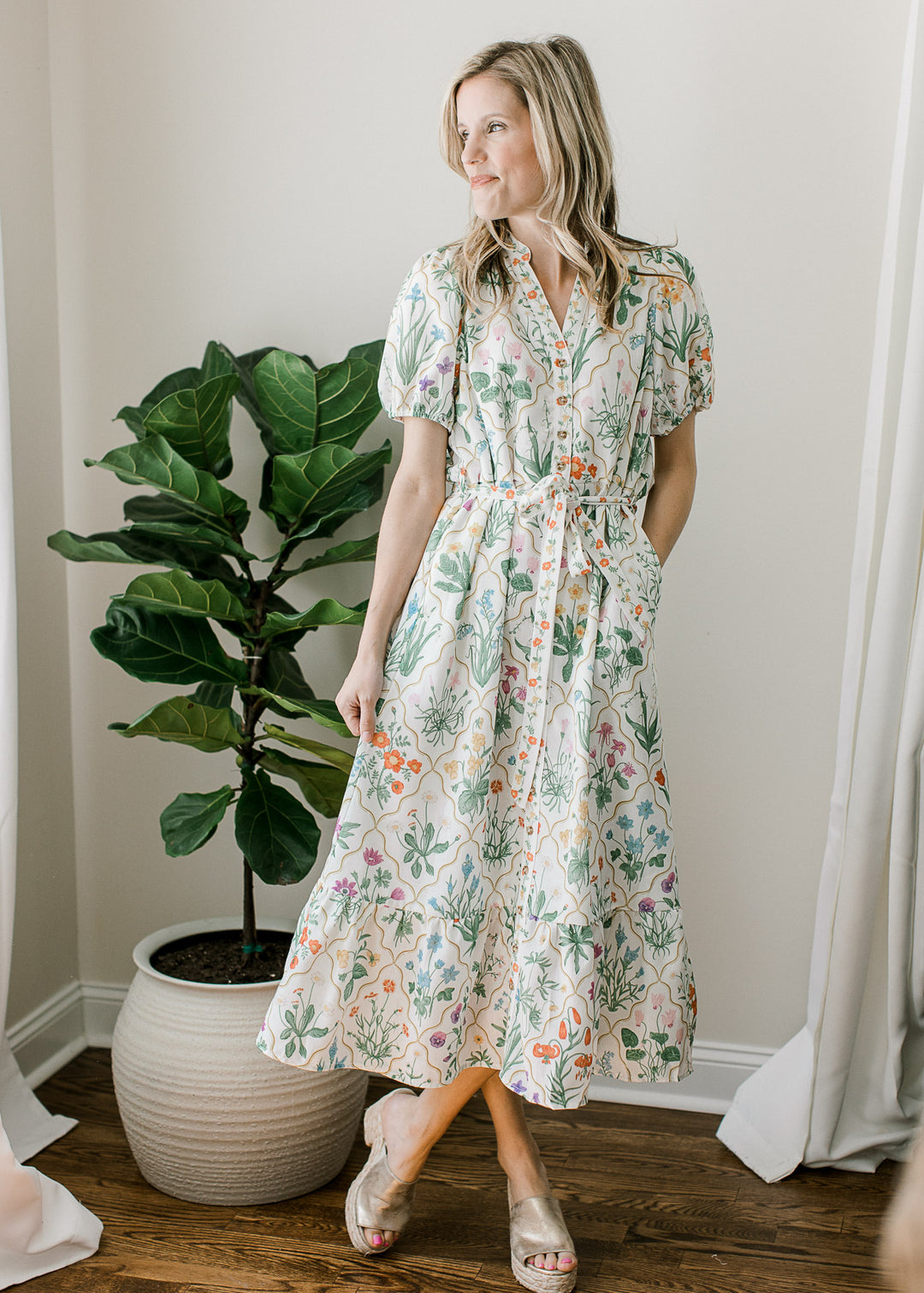 Model wearing an off white midi with bright floral pattern, buttons, short sleeves and pockets. 