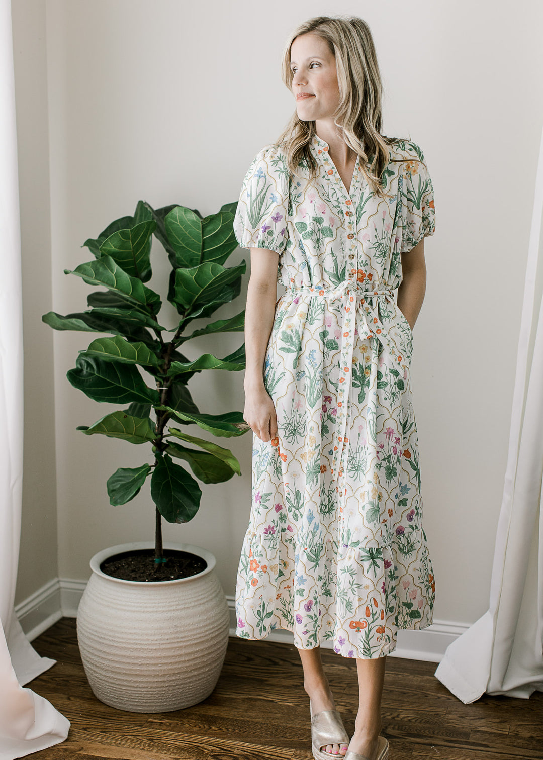 Model wearing heels and off white midi with floral pattern, buttons, short sleeves and pockets. 