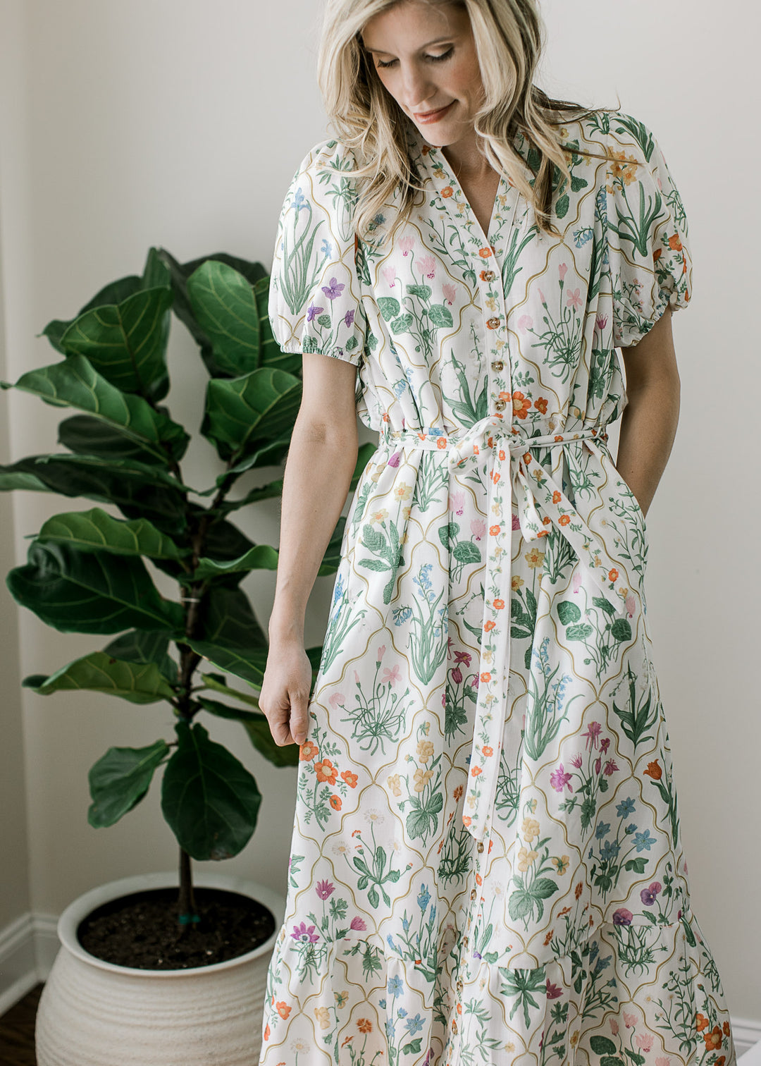 Close up of tie waist, button front and v-neck on an off white midi with bright floral pattern. 