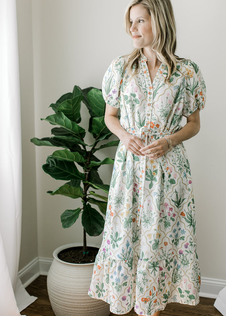 Model wearing an off white midi with bright floral, buttons, bubble short sleeves and pockets. 