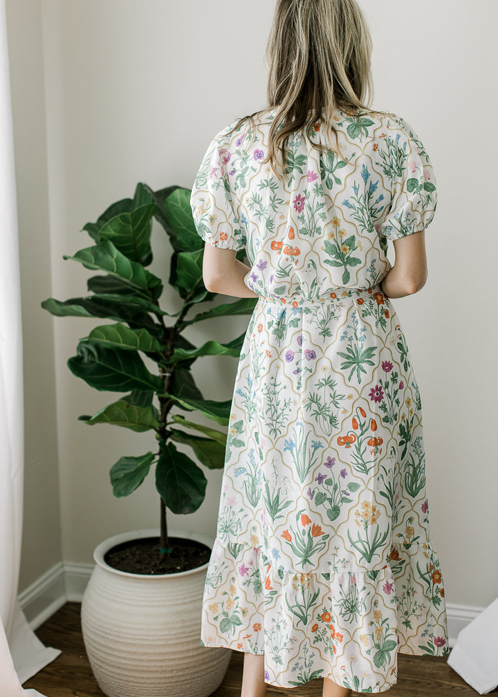Back view of model wearing an off white midi with bright floral pattern, buttons and short sleeves.