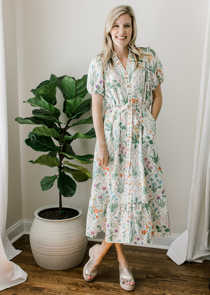 Model wearing an off white midi with bright floral, adjustable tie, short sleeves and pockets. 