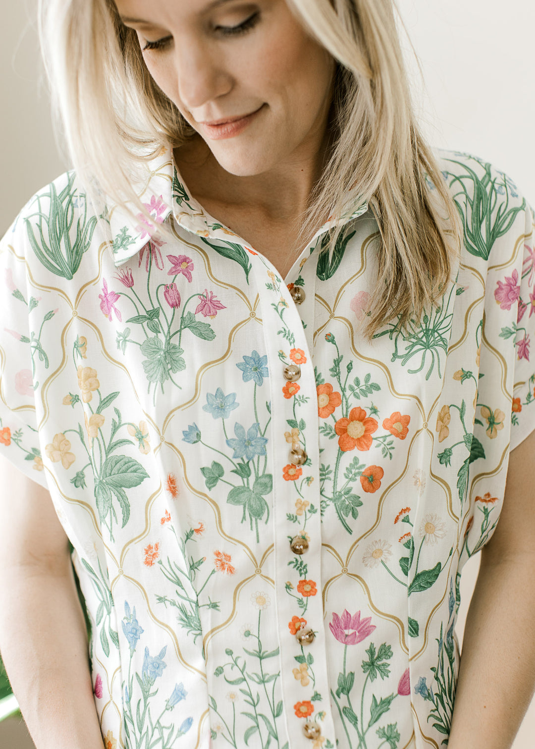 Close up of collar and buttons on a cream top with bright floral, and extended cap sleeves. 