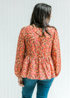 Back view of Model wearing a brick colored sheer long sleeve top with burgundy and copper floral. 
