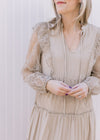 Close up of -neck with a tie and floral mesh long sleeves on a beige maxi with ruffle at shoulder.