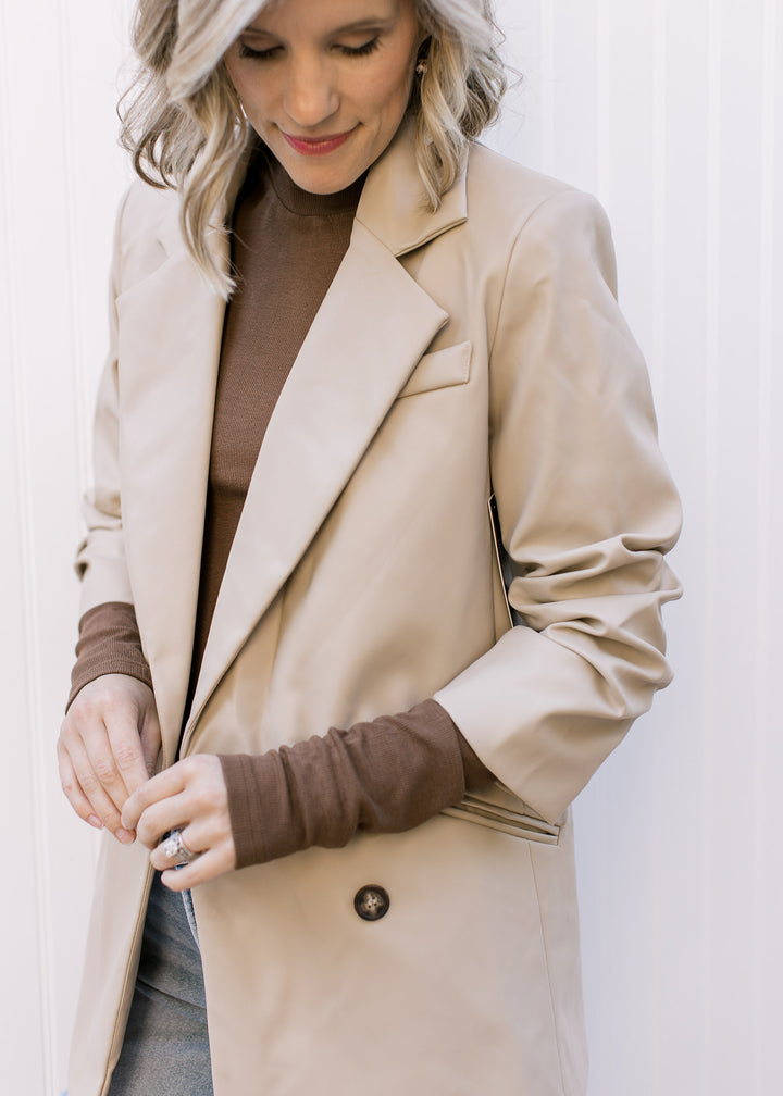 Model wearing a beige, faux leather jacket with double-breasted closure, collar and cinched sleeves.