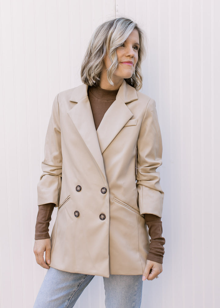 Model wearing a beige, faux leather jacket with double-breasted closure and 3/4 cinched sleeves.