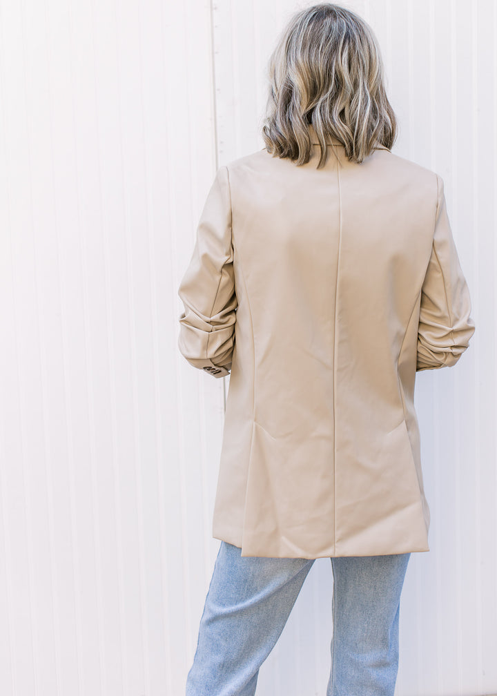 Back view of Model wearing a beige, faux leather jacket with flap collar and cinched sleeves.