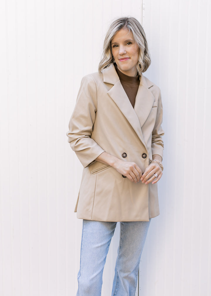 Model wearing jeans and a beige, faux leather jacket with double-breasted closure.