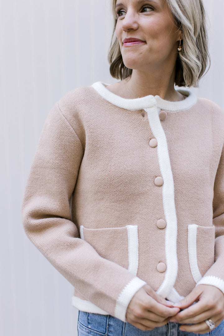Model wearing a beige button up cardigan with cream trim at the pockets, placket, cuffs, and neck.