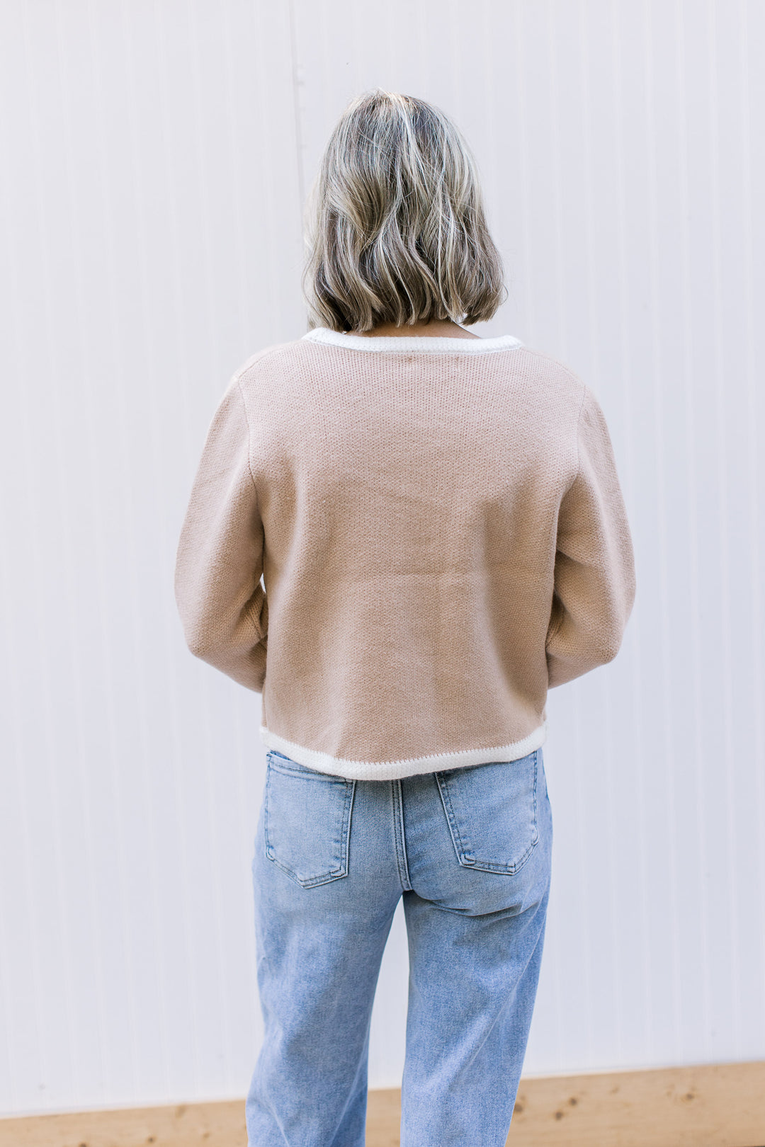 Back view of Model wearing a beige cardigan with cream trim, long sleeves and thick material.