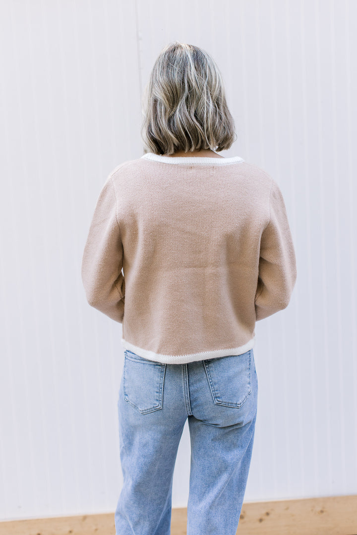 Back view of Model wearing a beige cardigan with cream trim, long sleeves and thick material.