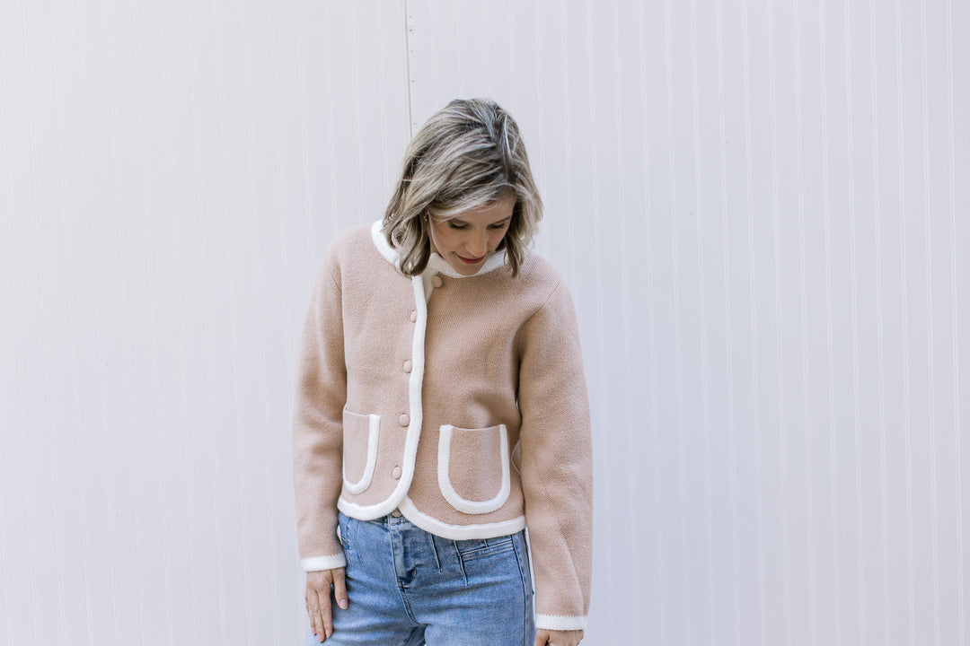 Model wearing jeans and a beige cardigan with cream trim at the pockets, placket, cuffs, and neck.