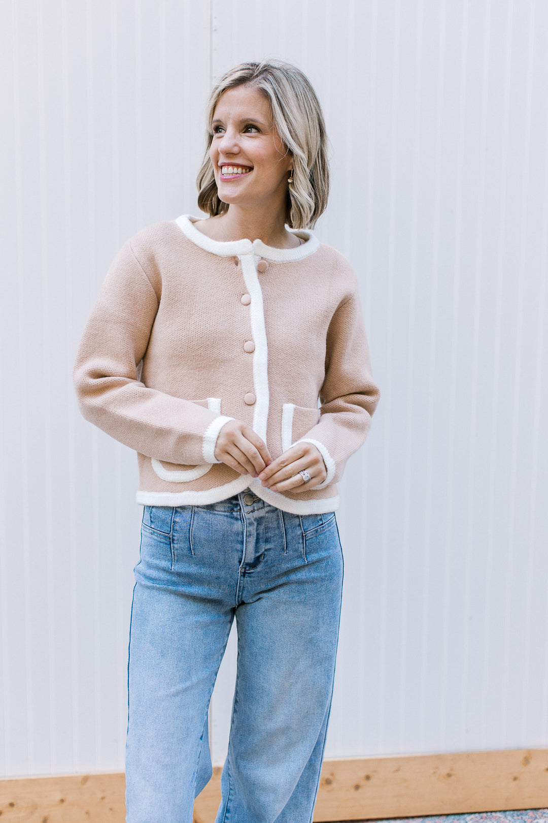 Model wearing a cozy beige button up cardigan with cream trim detail and long sleeves.