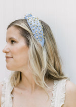 Side view of model wearing a blue bejeweled headband with a knotted fabric design. 