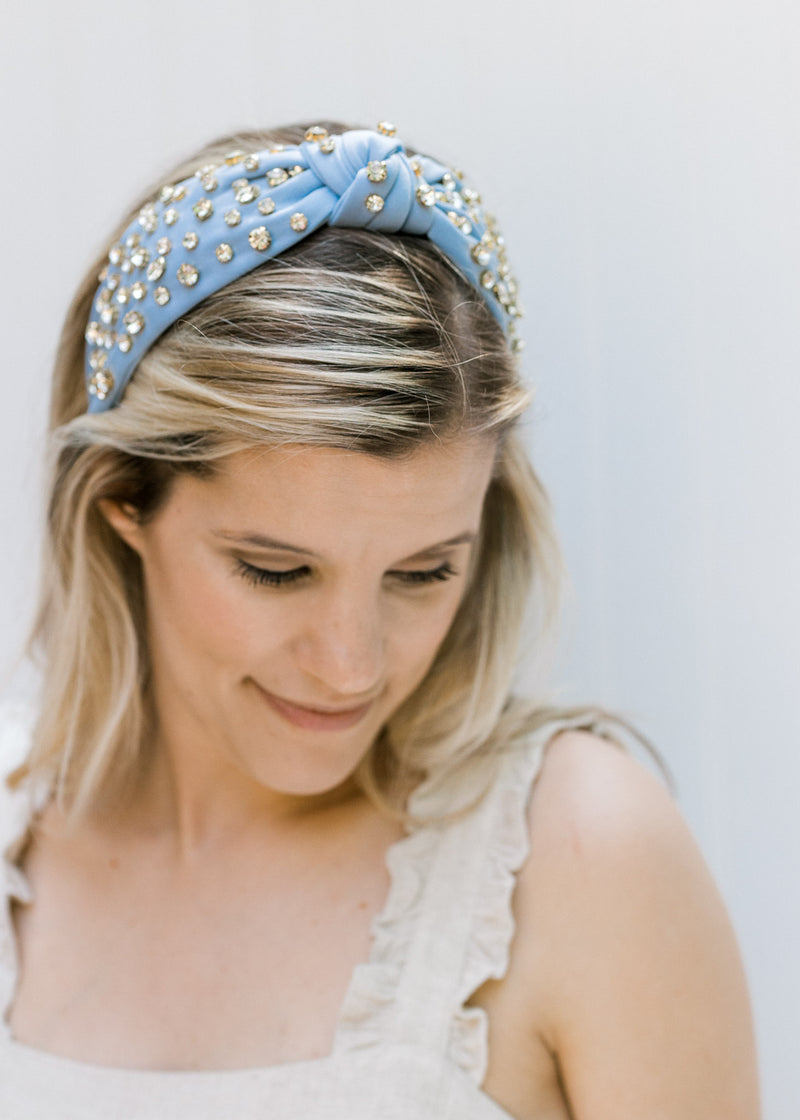 Model wearing a blue headband with a knotted fabric and rhinestones. 