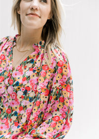 Close up of v-neck top with pink, mustard, light blue and green floral pattern and long sleeves. 