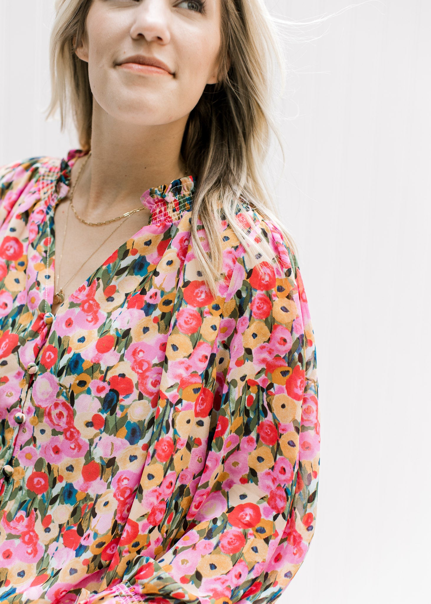 Close up of v-neck top with pink, mustard, light blue and green floral pattern and long sleeves. 