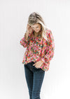 Model wearing jeans with a bright floral v-neck top with a smocked detail at the neck and wrist. 