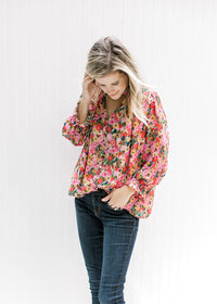 Model wearing jeans with a bright floral v-neck top with a smocked detail at the neck and wrist. 