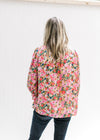 Back view of Model wearing a bright floral v-neck top with a smocked detail at the neck and wrist. 