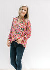 Model wearing a bright floral v-neck top with a smocked detail and ruffle at the neck and wrist. 