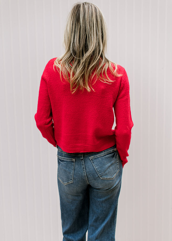 Back view of model wearing a bright red cardigan with a slightly cropped fit and long sleeves. 