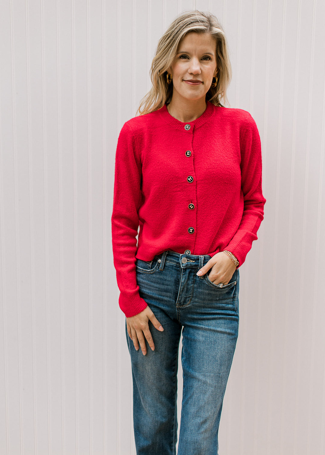 Model wearing a slightly cropped bright red button up cardigan with long sleeves and a round neck. 