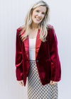 Model wearing a wine colored velvet blazer with long sleeves and a single button closure. 