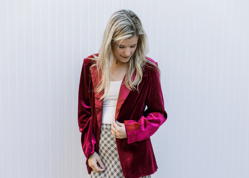 Model wearing a white top with a wine velvet blazer with long sleeves and a single button closure. 