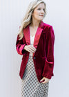 Model wearing a wine colored velvet blazer with long sleeves, faux pockets and flap collar. 