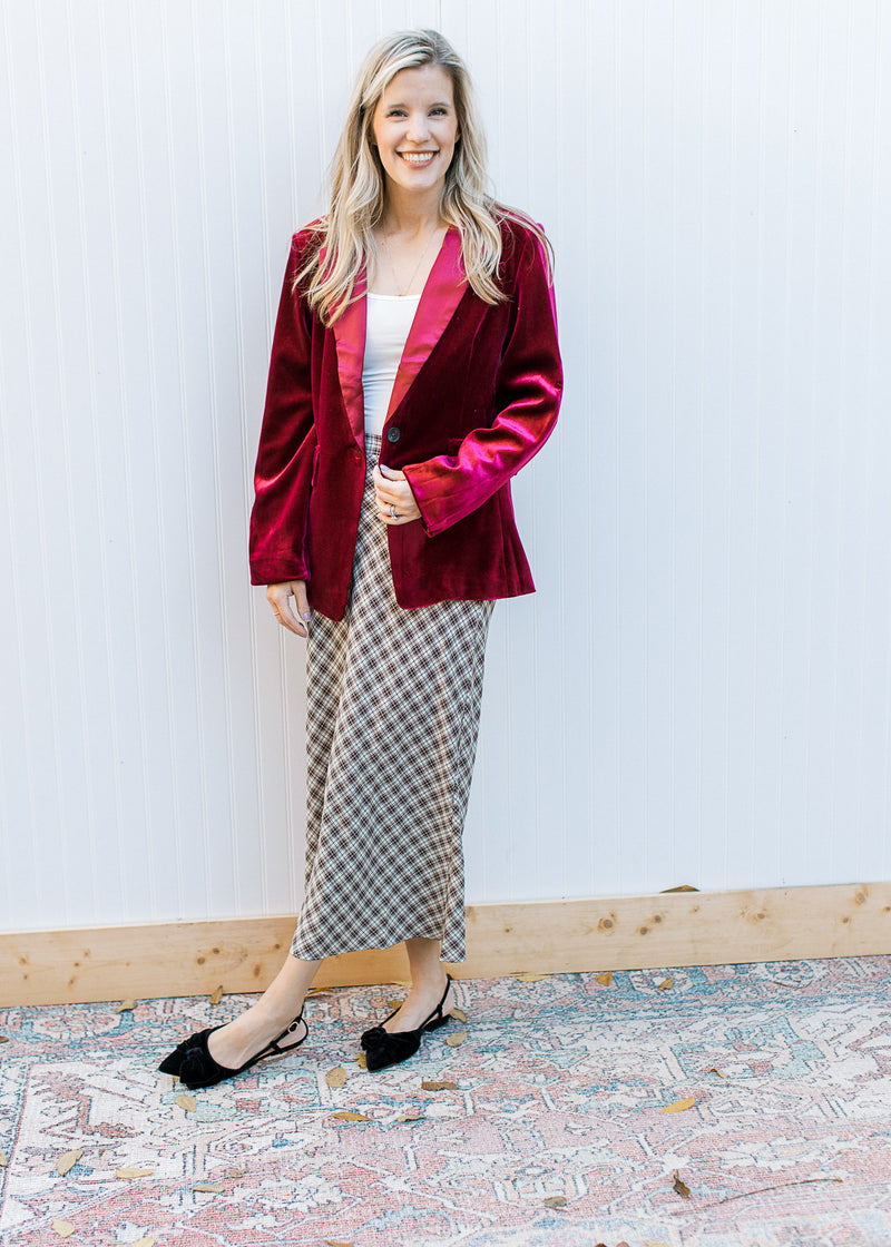 Model wearing a plaid skirt, flats and a  wine colored velvet blazer with long sleeves. 