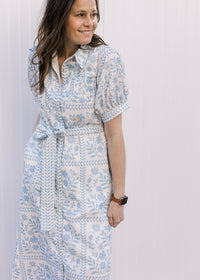 Model wearing a button front cream midi with pale blue floral, short sleeves and tie at the waist.