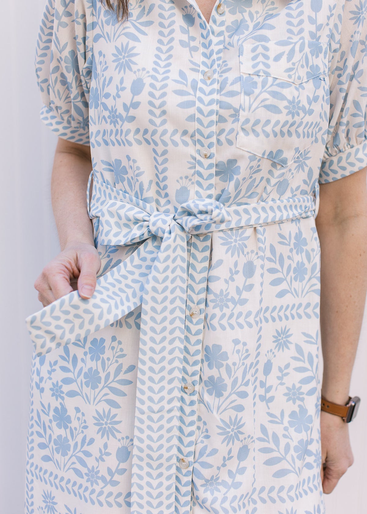 Close up of tie belt at the waist of a cream midi with pale blue floral and a button front. 