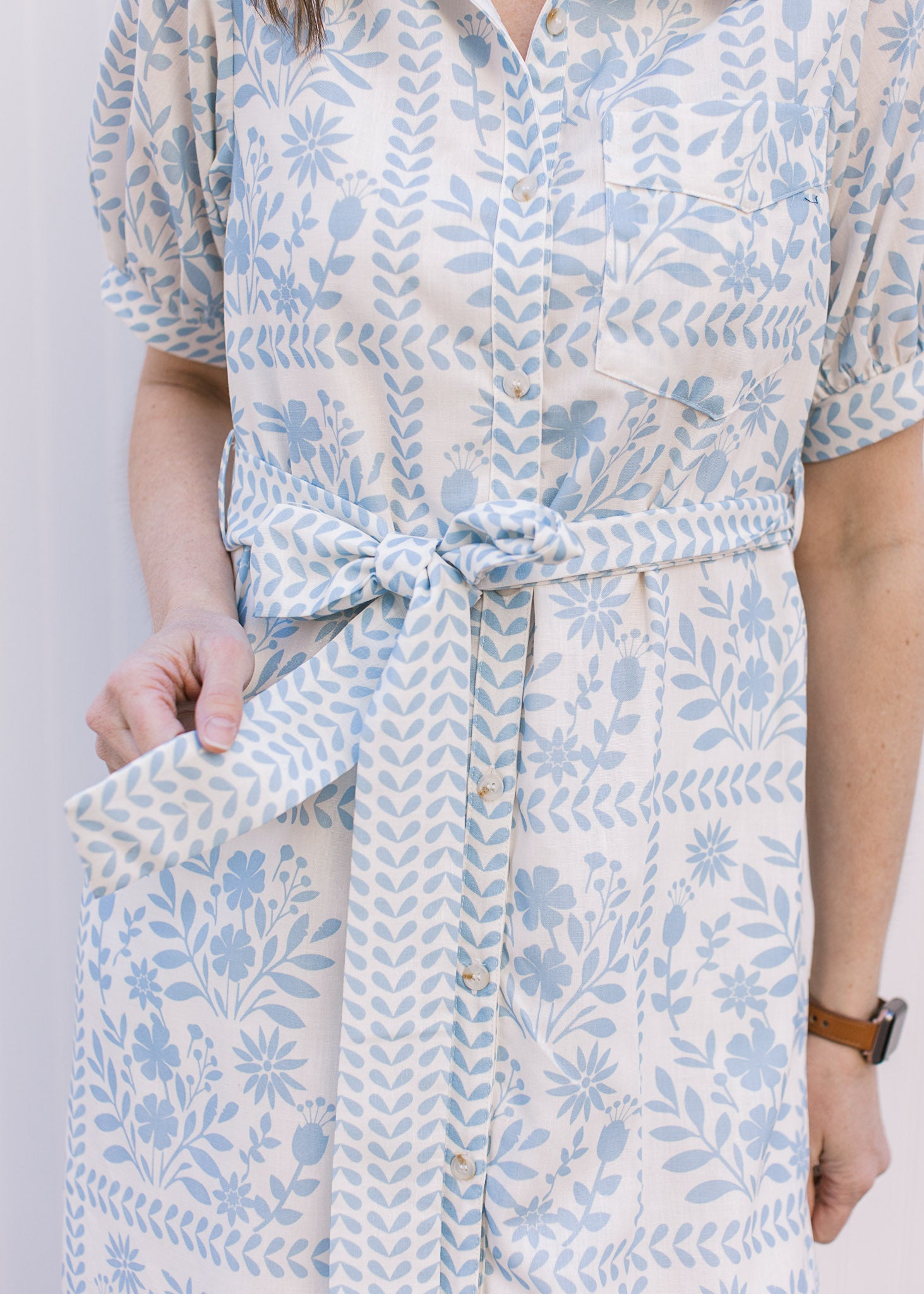 Close up of tie belt at the waist of a cream midi with pale blue floral and a button front. 