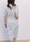 Back view of Model wearing a cream midi with pale blue floral, bubble short sleeves and tie belt.