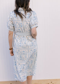 Back view of Model wearing a cream midi with pale blue floral, bubble short sleeves and tie belt.