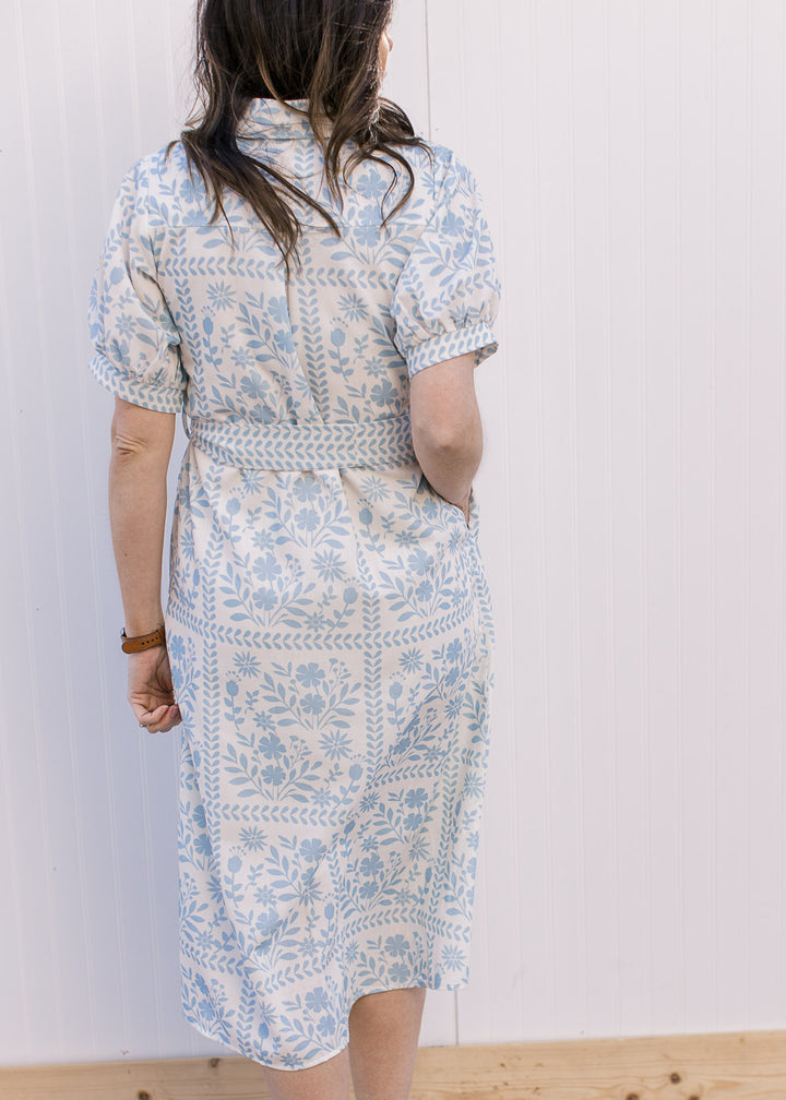Back view of Model wearing a cream midi with pale blue floral, bubble short sleeves and tie belt.