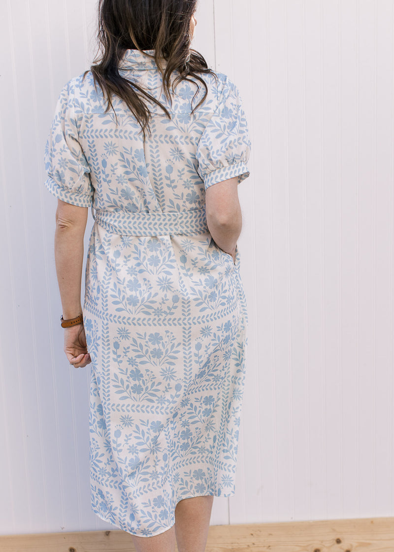Back view of Model wearing a cream midi with pale blue floral, bubble short sleeves and tie belt.