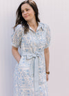 Model wearing a cream midi with pale blue floral, short sleeves, tie at the waist and a collar.