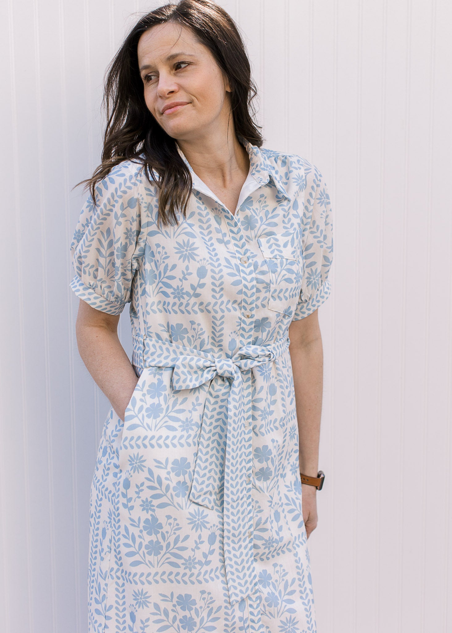 Model wearing a cream midi with pale blue floral, short sleeves, tie at the waist and a collar.