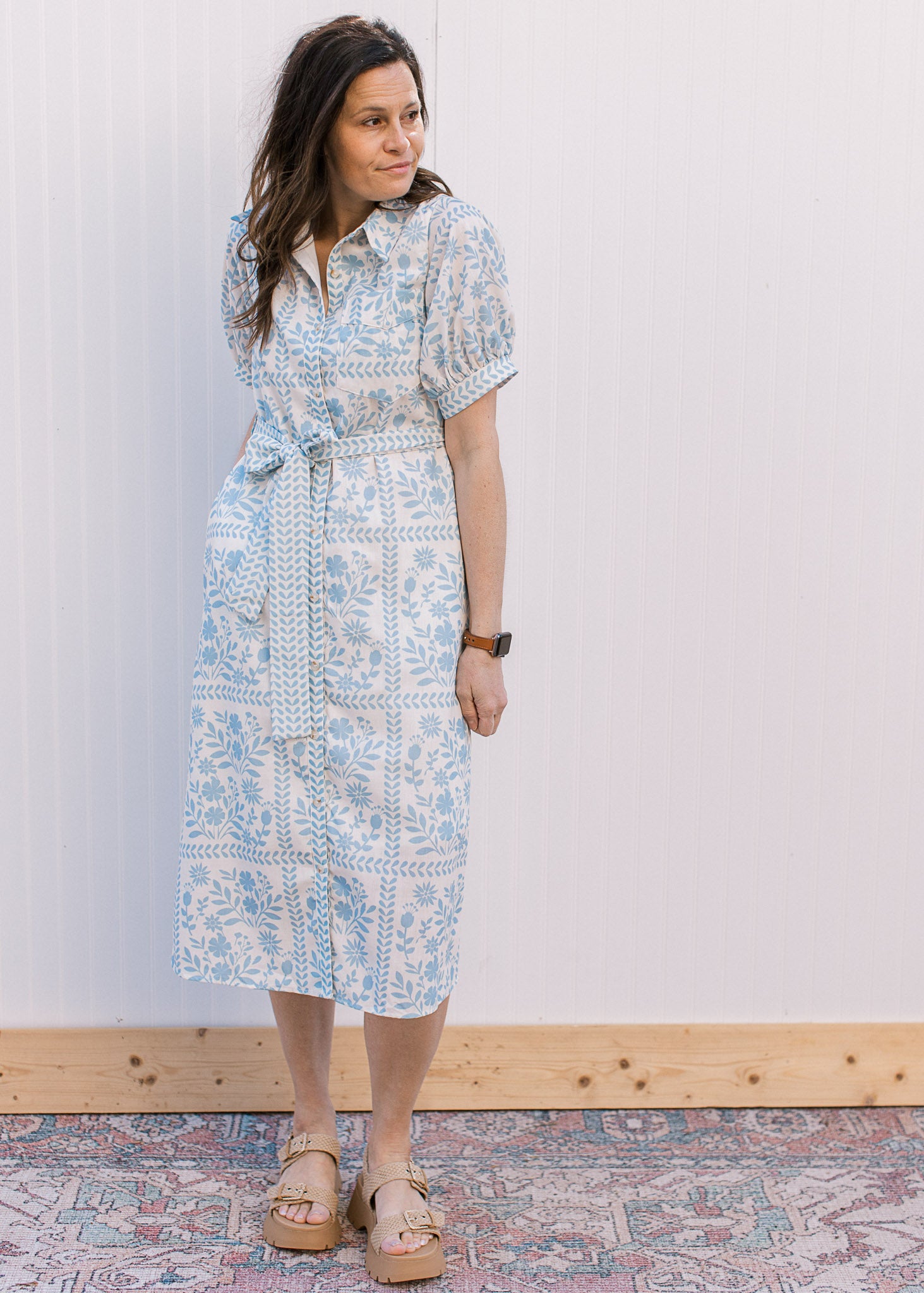 Model wearing sandals and a button front cream midi with pale blue floral and bubble short sleeves.