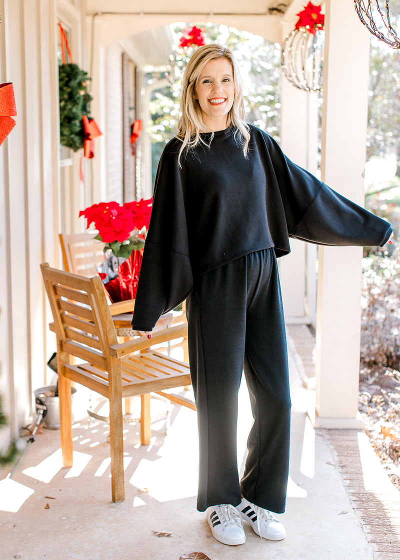 Model wearing a black sweater with matching pants with wide leg styling and elastic waist.