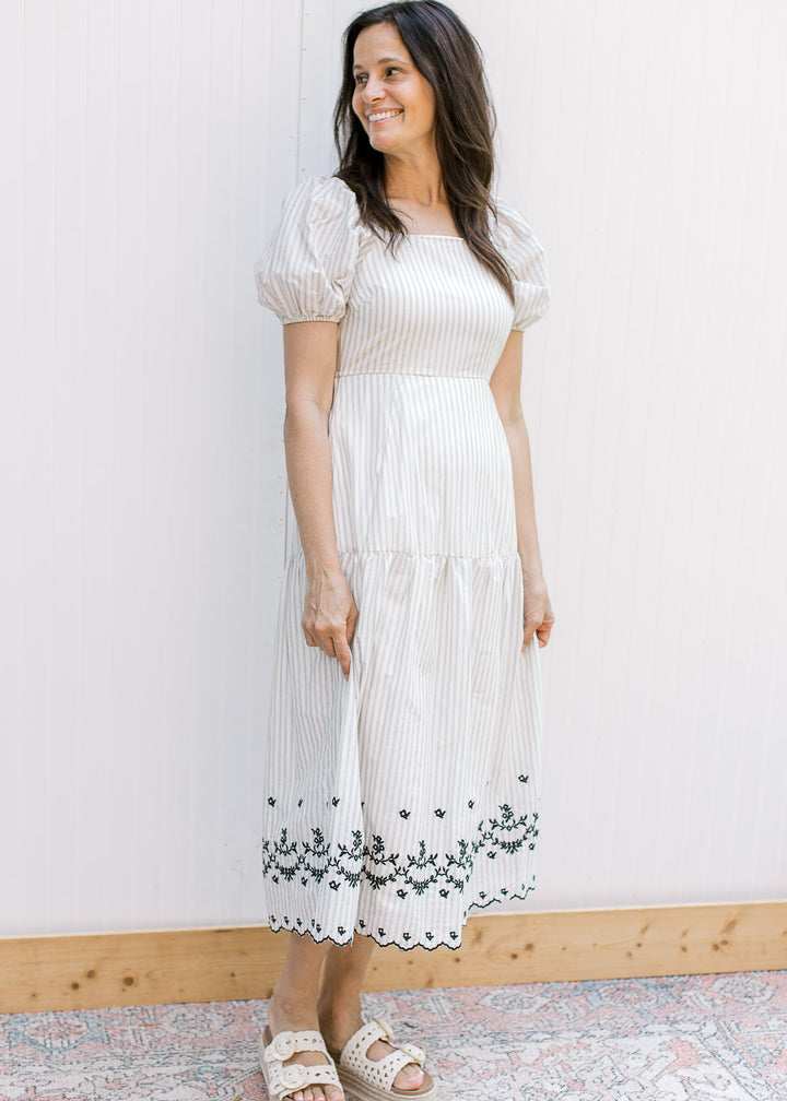 Model wearing a cream midi with gray stripes and black embroidered floral detail with scalloped hem.