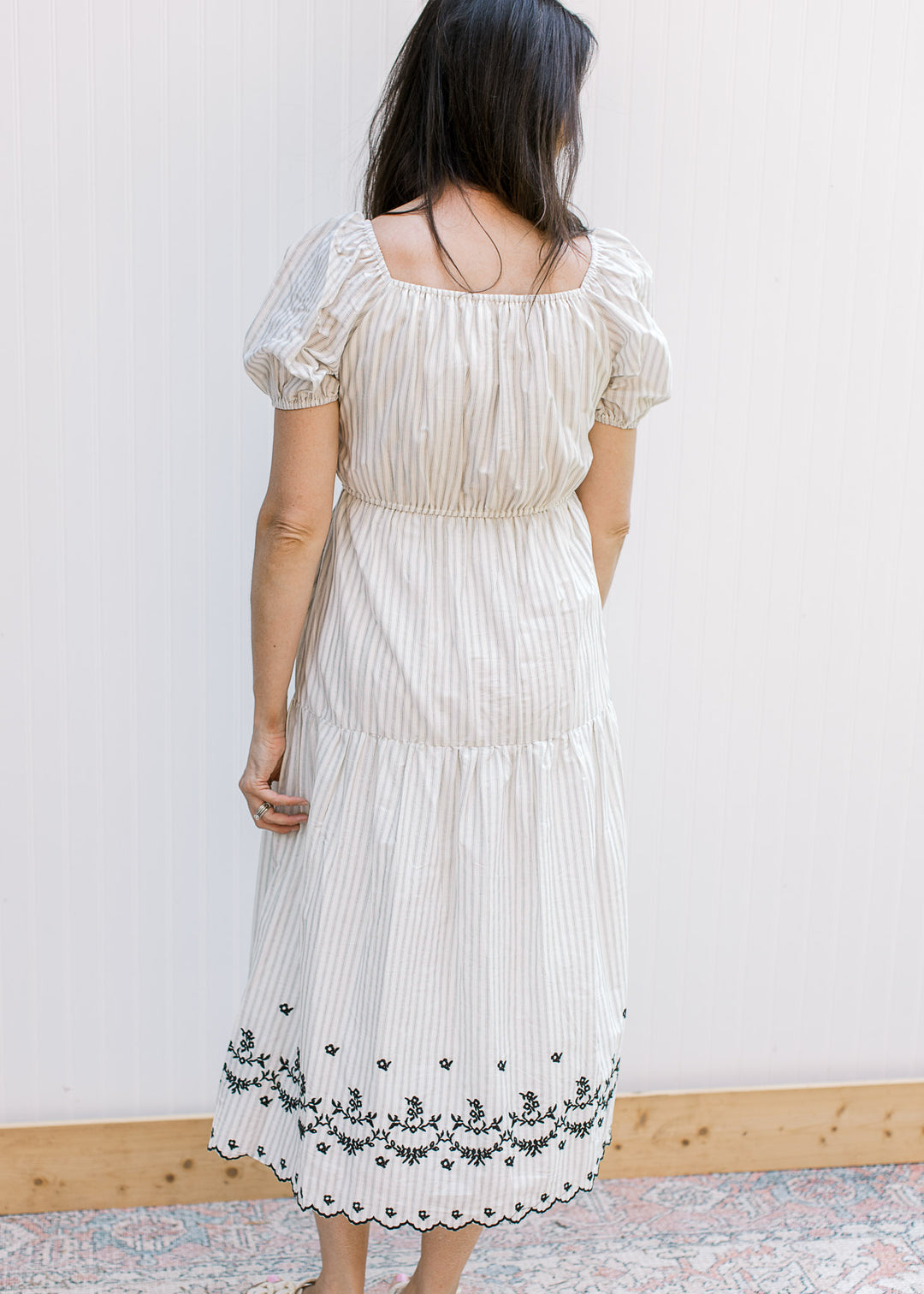 Back view of Model wearing a cream midi with gray stripes, square neck and elastic waistband.
