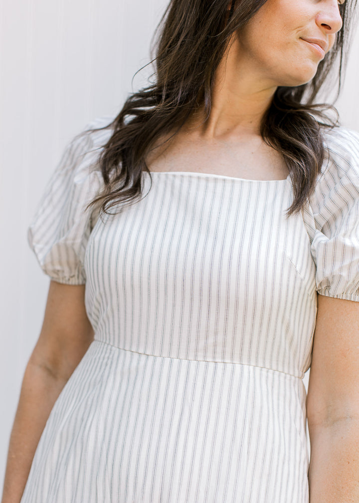 Close up of square neckline on a cream midi with gray stripes and bubble short sleeves. 