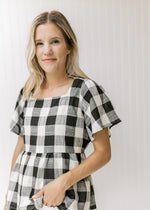 Model wearing a black and cream top with large scale gingham, a square neckline and short sleeves. 