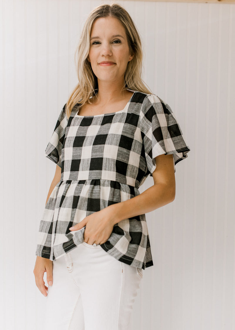 Model wearing white jeans with a black and cream top with large scale gingham and a square neckline.