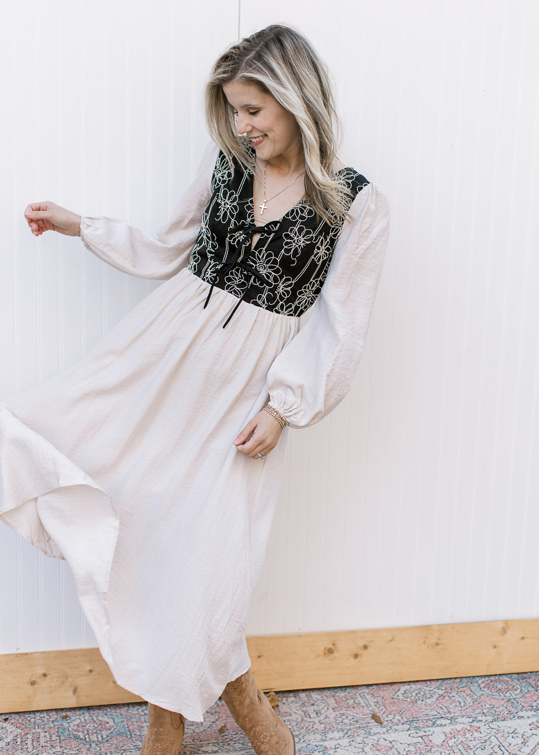 Model wearing an ivory dress with a black bodice, v-neck with ties and long sleeves.