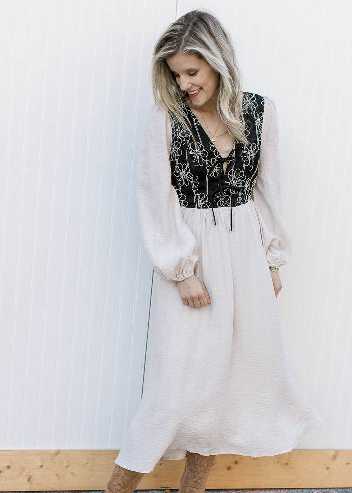Model wearing a flowy ivory midi with a black bodice with ivory floral, v-neckline and long sleeves.